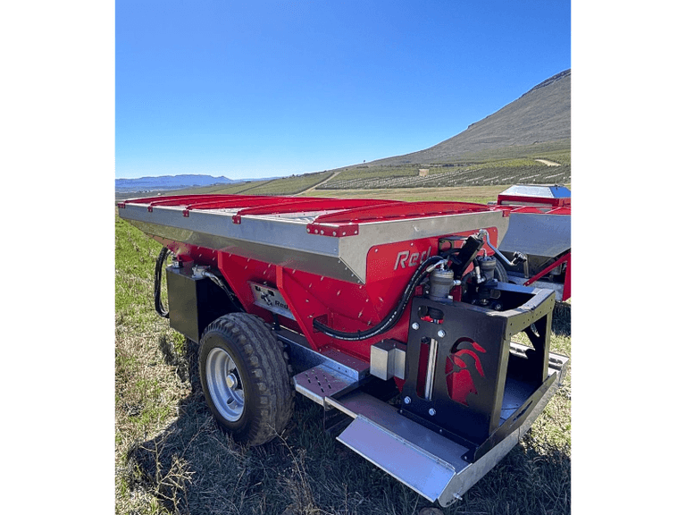 Red Ant spreader standing in a field below the mountains